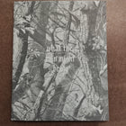 A square art print or book cover featuring a grayscale camouflage-style forest tree pattern with the text 'what the rain might bring' in the center, placed on a brown textured surface.